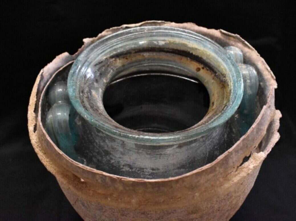 A Roman glass urn in a clay shell against a black background