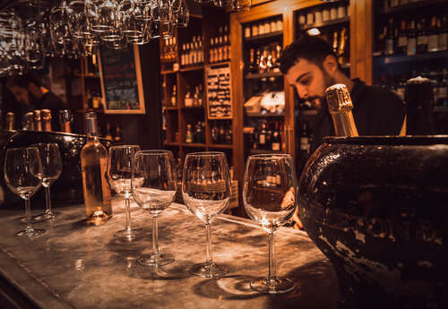A barman in a Madrid wine ba with pictures on the wall behind him and empty wine glasses on the bar in front of him