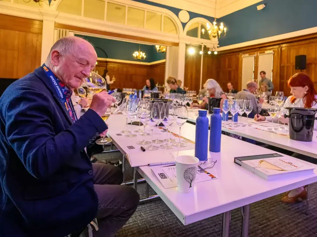 Tasters at the Battle of the Bubbles sitting at a white table sniffing glasses of Champagne and taking notes