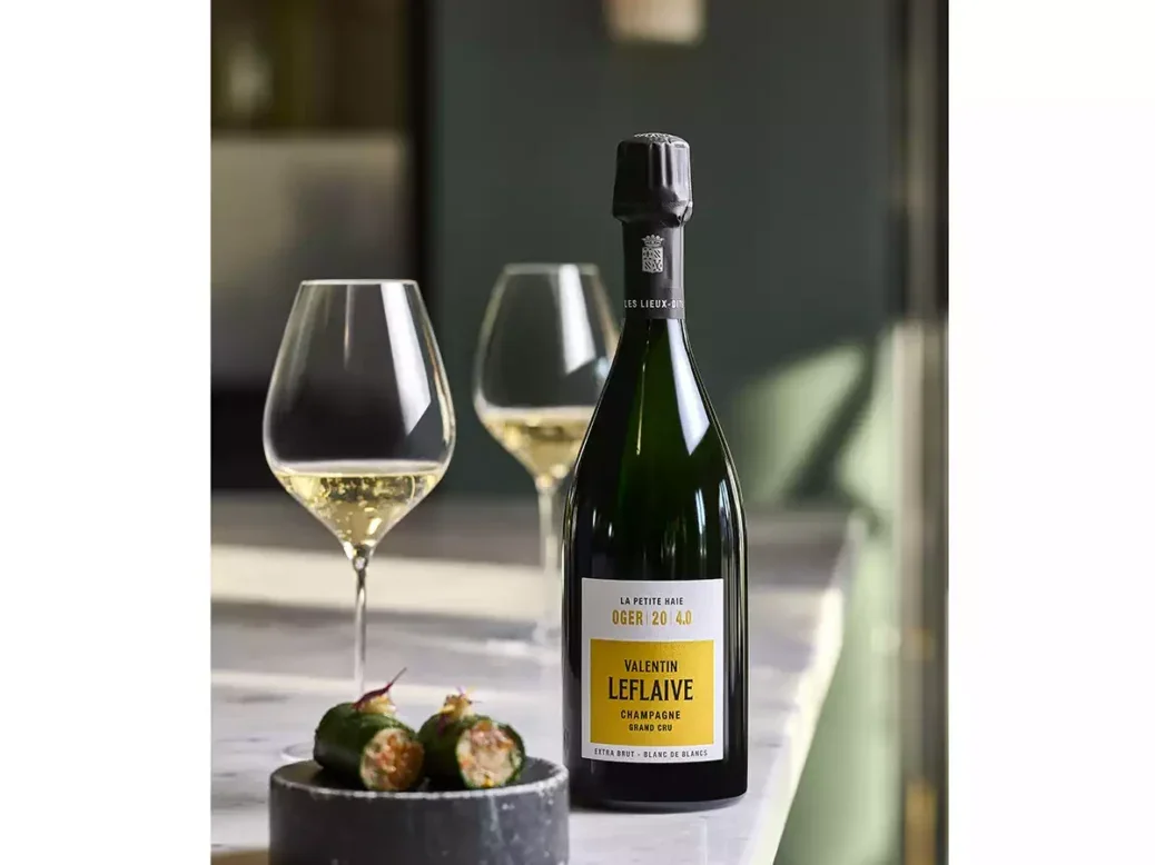 A bottle of Valentin Leflaive Champagne with two glasses on a white table.