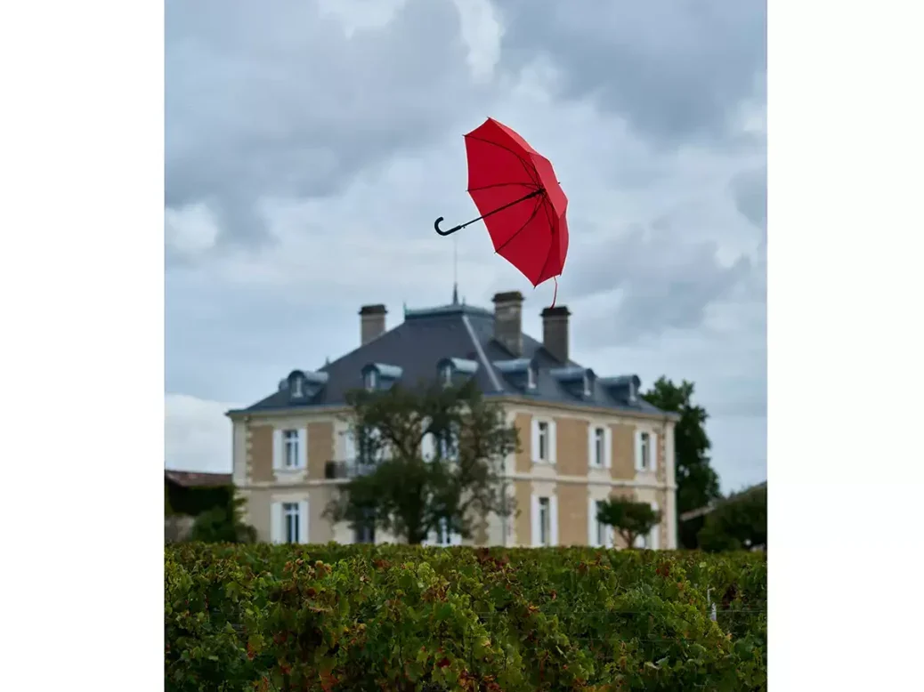 A page in Château Haut-Bailly’s 2024 Bordeaux en primeur catalogue, Singing in the Rain, with a red umbrella flying above the vines in front of the château