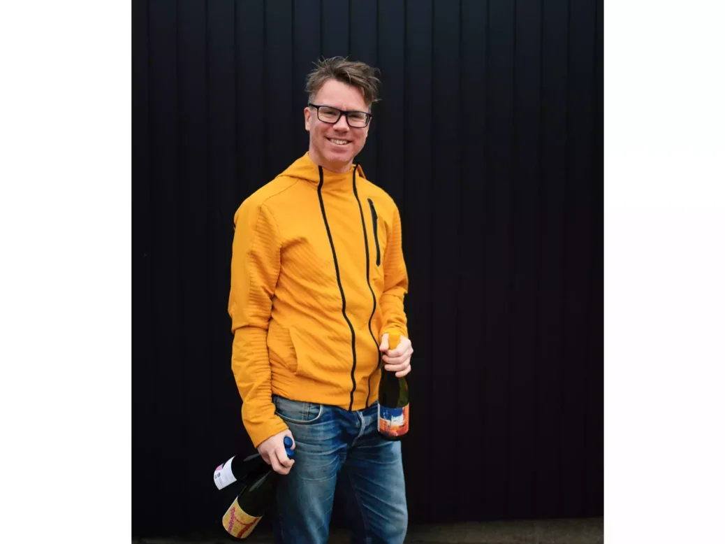 Chris Wilson of Gutter & Stars in an orange jacket holding a bottle of wine