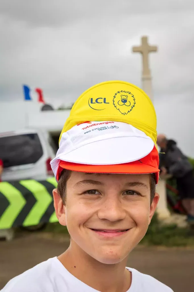 A smiling boy in a white t-shirt wearing three caps, the top white, the middle yellow, the bottom red/orange